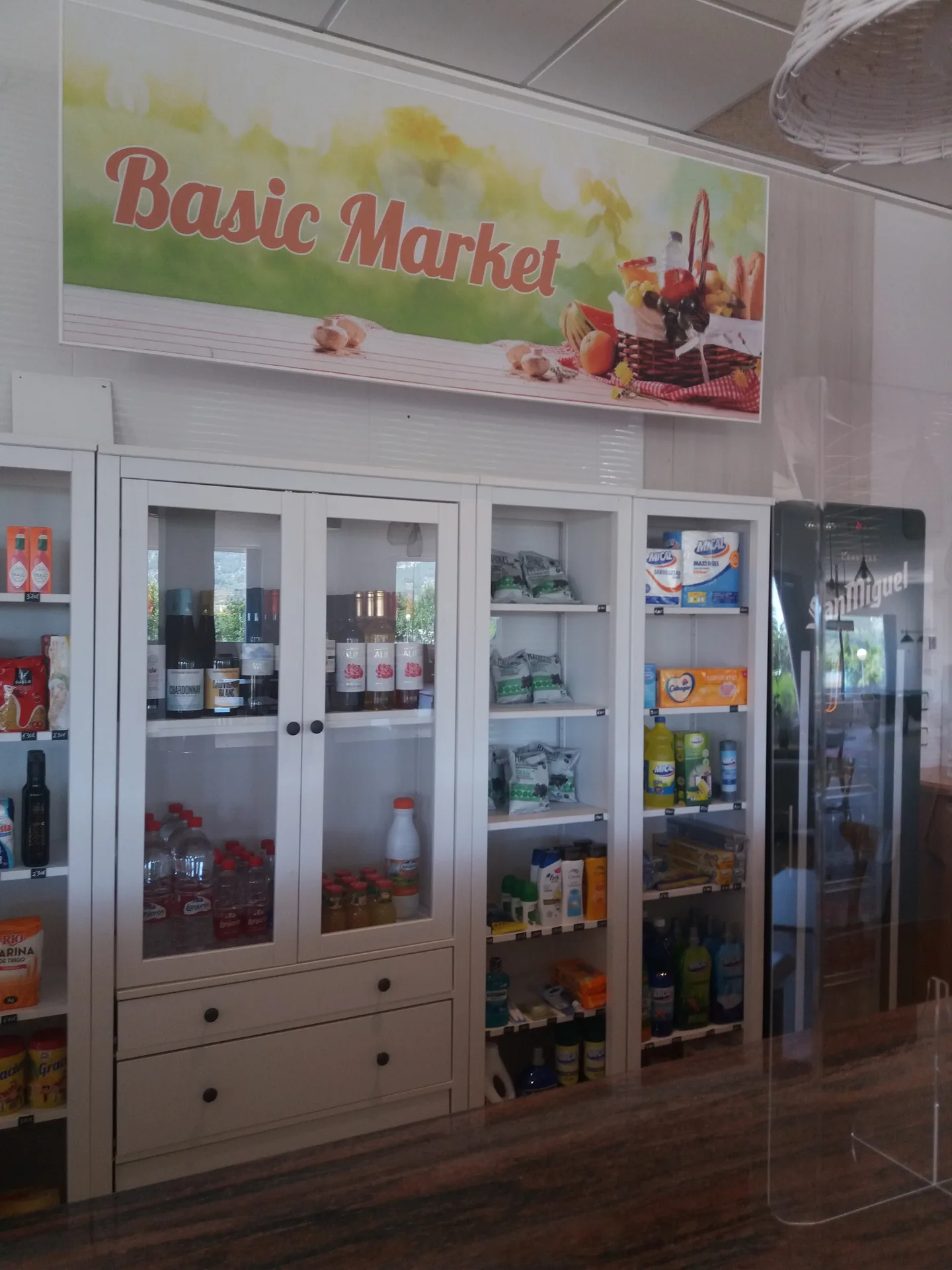 Interior de minimercado del camping con estanterías de productos y cartel 'Basic Market'.