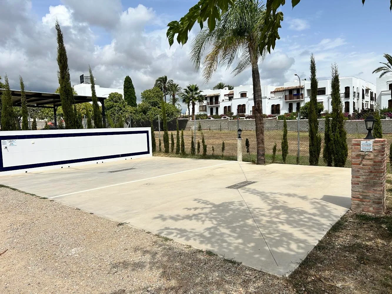 Área de autocaravanas con explanada pavimentada, fuente/servicios y edificio residencial al fondo.