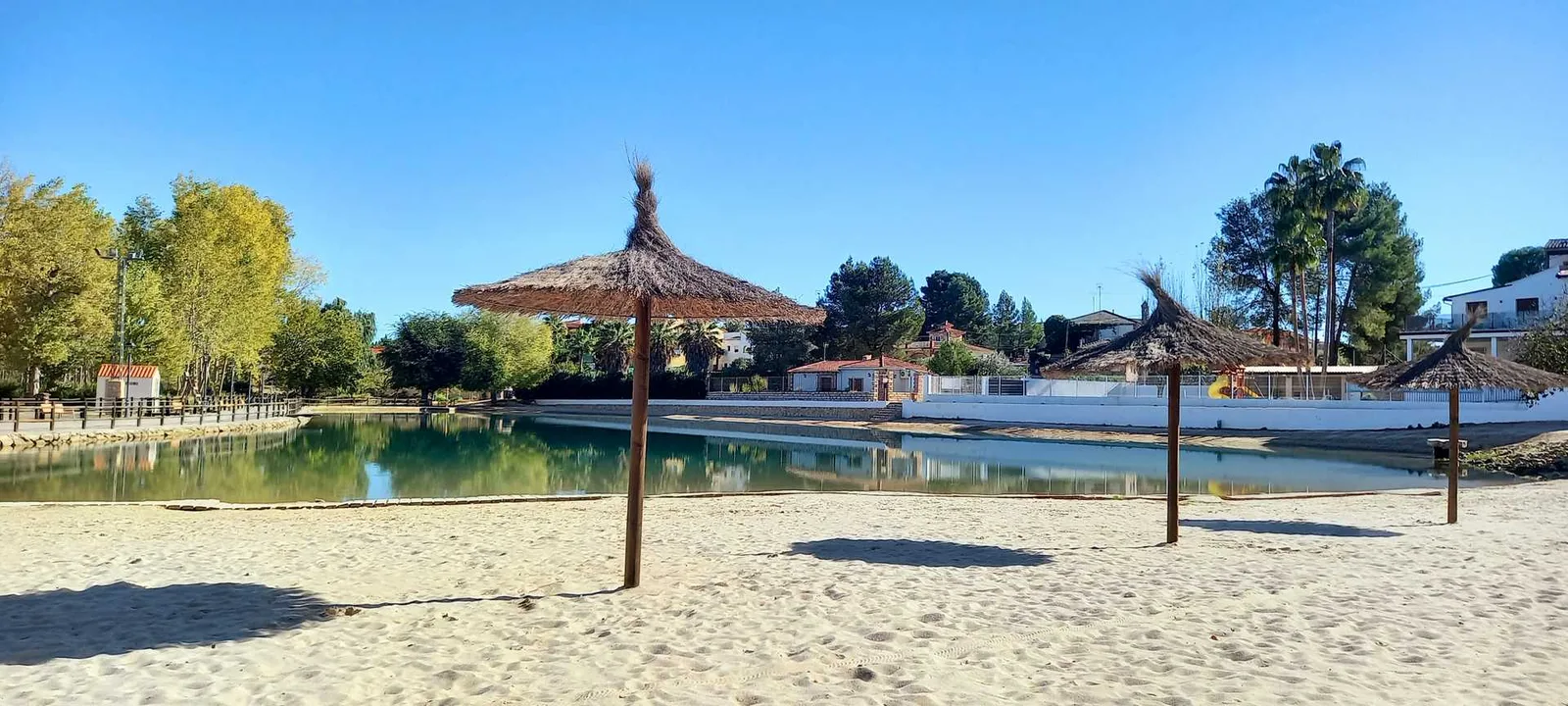 Lago de Playamonte con su playa de arena y sombrillas de paja, junto al camping de Navarrés
